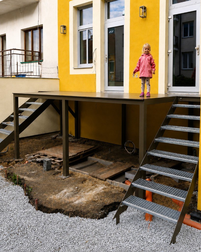 Kovová konstrukce terasy při stavbě u žluté fasády